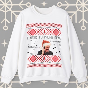 May include: White Christmas sweater with a red and white pattern. The sweater features a picture of a man wearing a Santa hat and talking on a phone. The text on the sweater reads "I need to phone Gene".