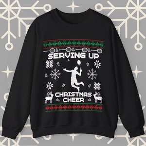 Op de afbeelding: Zwarte kersttrui met een wit silhouet van een badmintonner en de tekst "Serving Up Christmas Cheer".