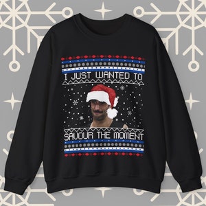 Può includere: Maglione natalizio nero con un motivo a fiocco di neve bianco, rosso e blu. Il maglione presenta un uomo con un cappello da Babbo Natale e il testo "Volevo solo assaporare il momento".