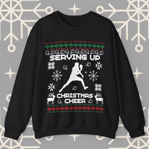 Op de afbeelding: Zwarte kersttrui met een wit silhouet van een persoon die tennis speelt en de tekst "Serving Up Christmas Cheer".