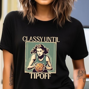 Op de afbeelding: Zwart T-shirt met een vintage-stijl grafische afbeelding van een vrouw die een basketbal dribbelt. De afbeelding zegt "Classy Until Tipoff".