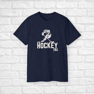 Puede incluir: Camiseta azul marino con un gr&aacute;fico blanco de un jugador de hockey patinando y el texto "In My Hockey Era".