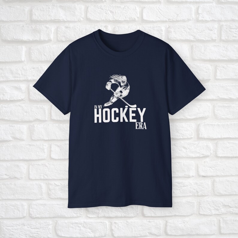 Puede incluir: Camiseta azul marino con un gr&aacute;fico blanco de un jugador de hockey patinando y el texto "In My Hockey Era".