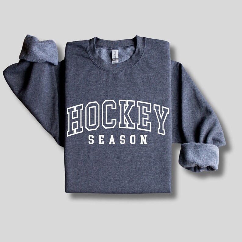 Pu&ograve; includere: Una felpa grigia scura con il testo "HOCKEY SEASON" in lettere bianche con contorno.