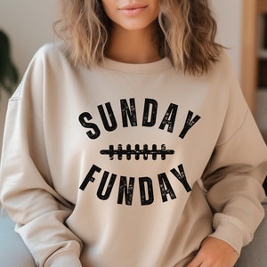 Op de afbeelding: Een beige sweatshirt met een zwarte grafische print die "SUNDAY FUNDAY" zegt met een voetbalnaadontwerp.