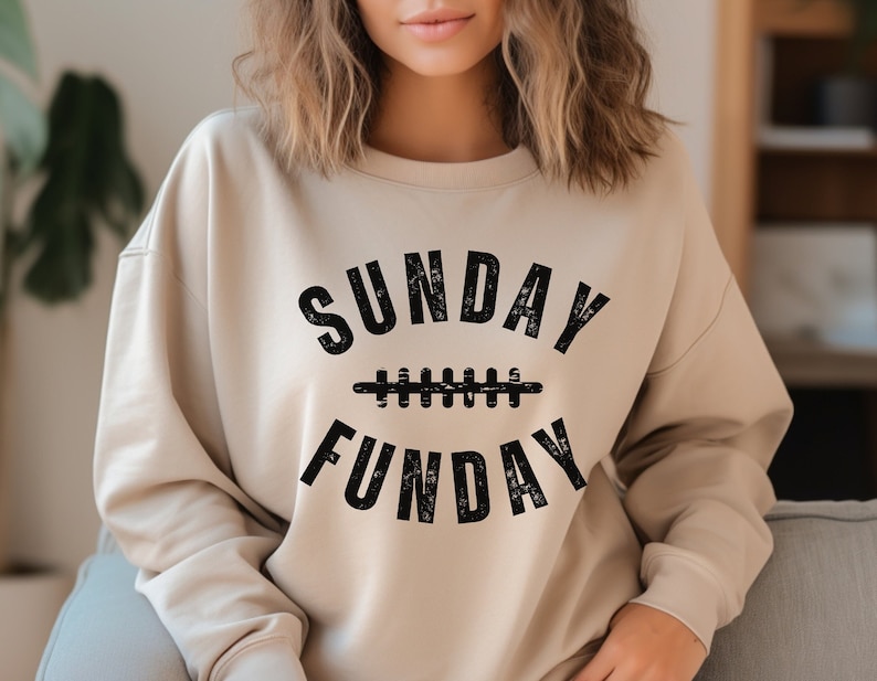 Op de afbeelding: Een beige sweatshirt met een zwarte grafische print die "SUNDAY FUNDAY" zegt met een voetbalnaadontwerp.