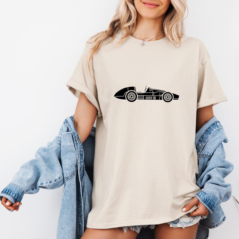 Puede incluir: Una camiseta beige con una silueta negra de un coche de carreras vintage impreso en la parte delantera.