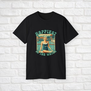 May include: Black t-shirt with a retro-style graphic of a woman in a swimsuit sitting by a pool. The graphic says "Happiest in the water".