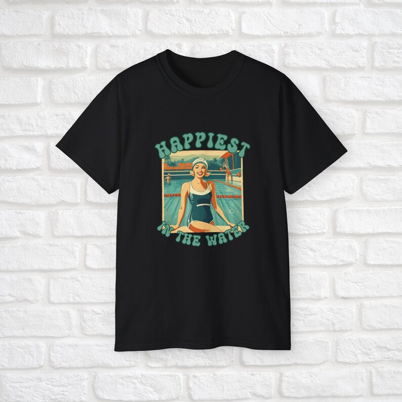 May include: Black t-shirt with a retro-style graphic of a woman in a swimsuit sitting by a pool. The graphic says "Happiest in the water".