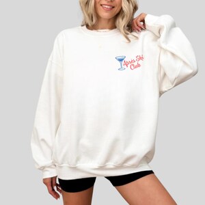 May include: White sweatshirt with a blue and red graphic of a martini glass and the text "Apr&egrave;s Ski Club".