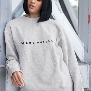 May include: A gray sweatshirt with the text "MAKE PUTTS" printed on the front.