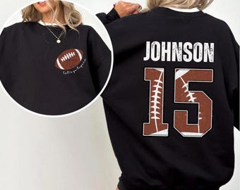 May include: Black sweatshirt with a white collar. It has a brown and white football graphic on the front and the name "JOHNSON" and the number "15" on the back.