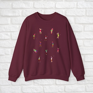 May include: Burgundy sweatshirt featuring a design of women playing golf. The women are depicted in various poses and wearing different coloured clothing.