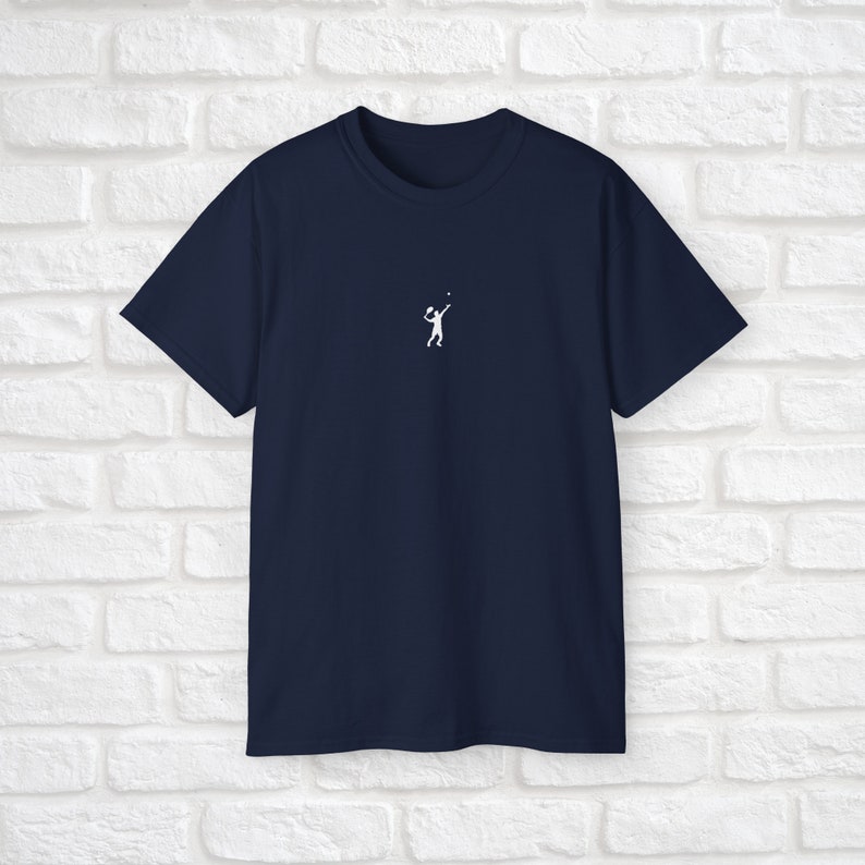 Pu&ograve; includere: Una t-shirt blu navy con una silhouette bianca di una persona che gioca a tennis.