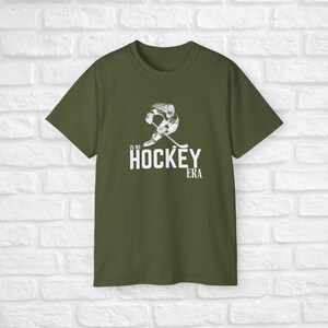 Puede incluir: Una camiseta verde con un gr&aacute;fico blanco de un jugador de hockey patinando y el texto "In My Hockey Era".