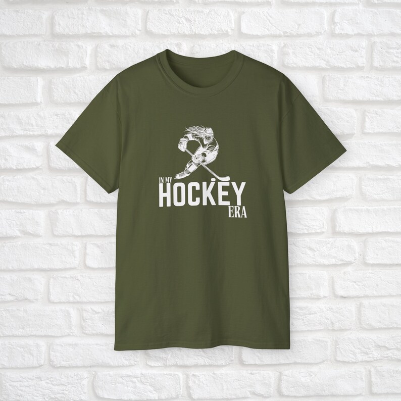 Puede incluir: Una camiseta verde con un gr&aacute;fico blanco de un jugador de hockey patinando y el texto "In My Hockey Era".