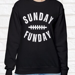 Op de afbeelding: Zwart sweatshirt met witte tekst die "SUNDAY FUNDAY" luidt met een voetbalafbeelding tussen de woorden.