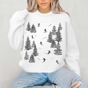 May include: White sweatshirt with a black and white graphic print of skiers and pine trees.