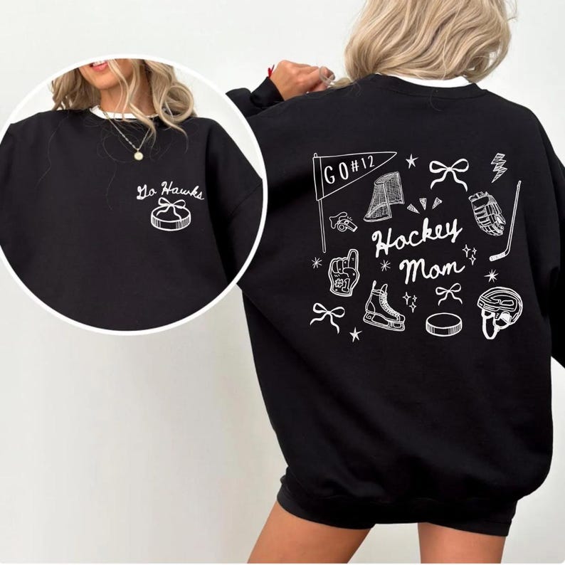 Woman wearing a crewneck sweatshirt with “Hockey Mom” doodle graphic on the back and personalized team name "Go Hawks" and player number "12" on the front; casual hockey game day outfit for moms.