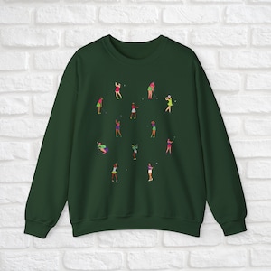 May include: A dark green sweatshirt featuring a design of women playing golf. The women are depicted in various poses and wearing different coloured clothing.