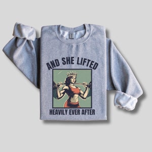 May include: Gray sweatshirt with a graphic of a woman wearing a crown and lifting weights. The text "And she lifted heavily ever after" is printed below the graphic.