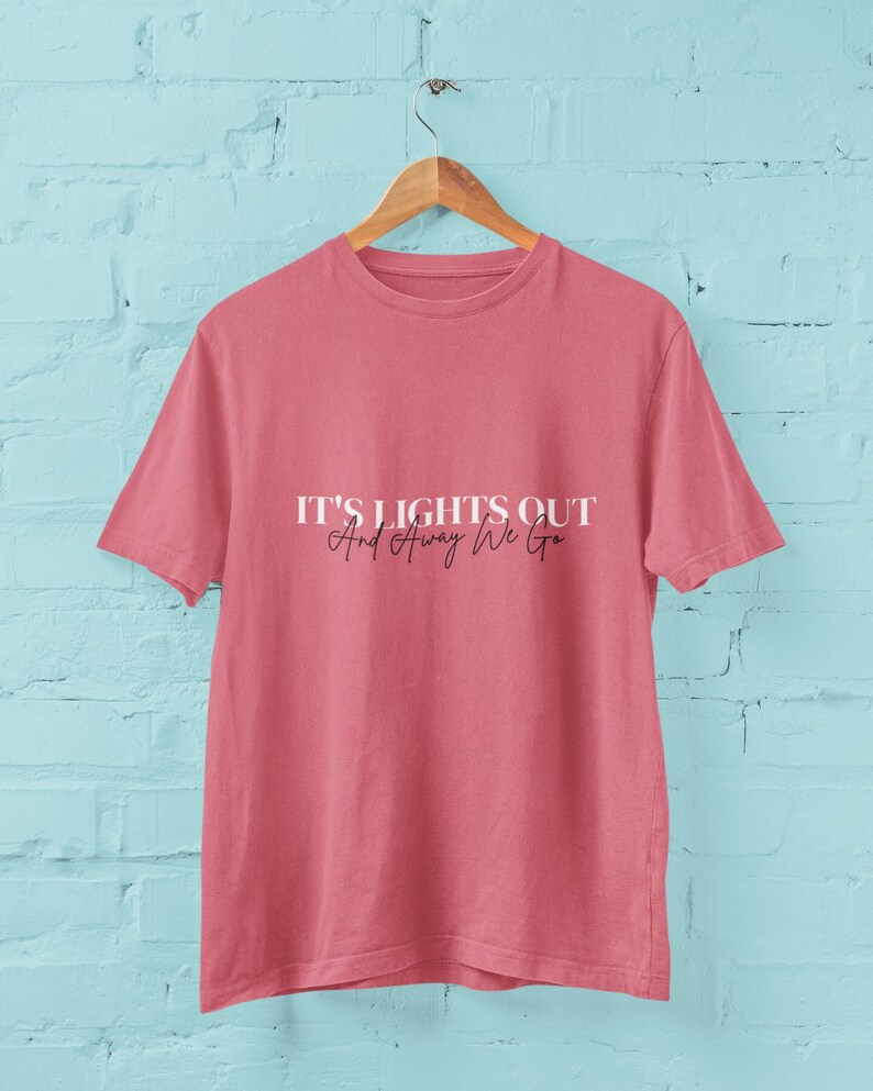 Puede incluir: Una camiseta rosa con el texto "It's Lights Out And Away We Go" impreso en la parte delantera en blanco.