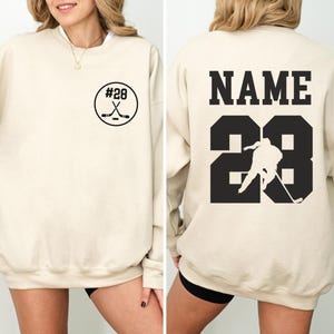 Custom hockey sweatshirt featuring a personalized hockey player name and number design on the back as well as jersey number on the front design.  Also, choose from a variety of hockey player silhouettes to further customize this hockey sweater