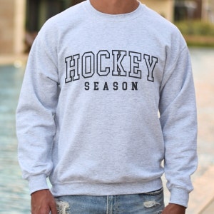 Pu&ograve; includere: Una felpa grigia con la scritta "HOCKEY SEASON" stampata in nero.