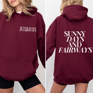 maroon golf themed hoodie with sunny days and fairways in a bold, trendy font on the back of the shirt. On the front, is a small sunny days and fairways graphic on the left chest