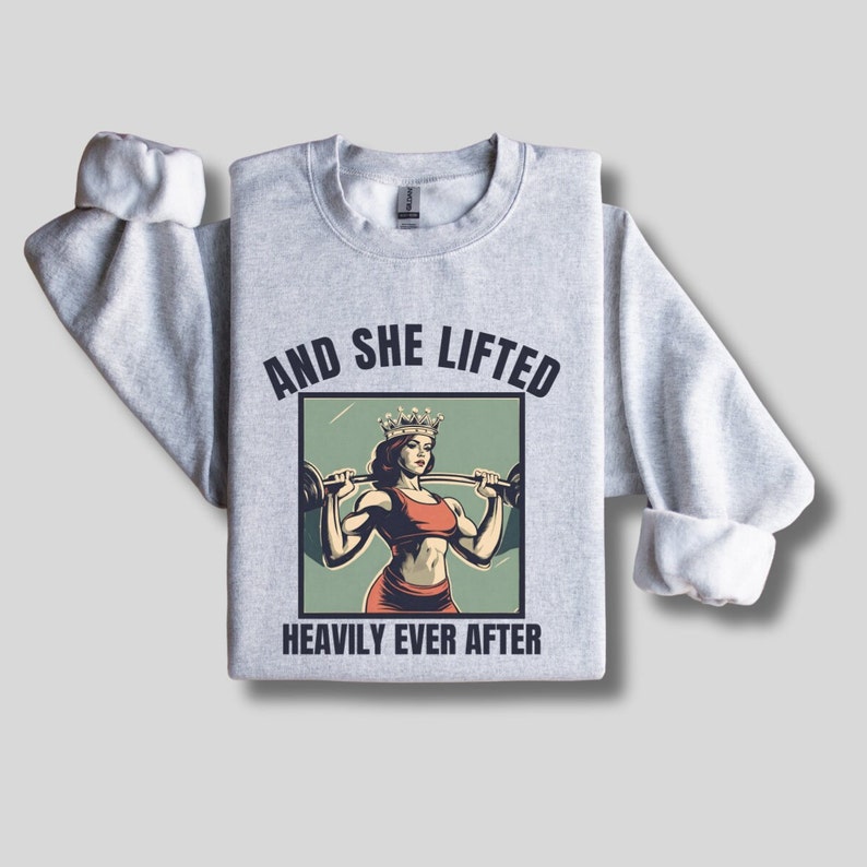 May include: Gray sweatshirt with a graphic of a woman wearing a crown and lifting weights. The text "And she lifted heavily ever after" is printed below the graphic.