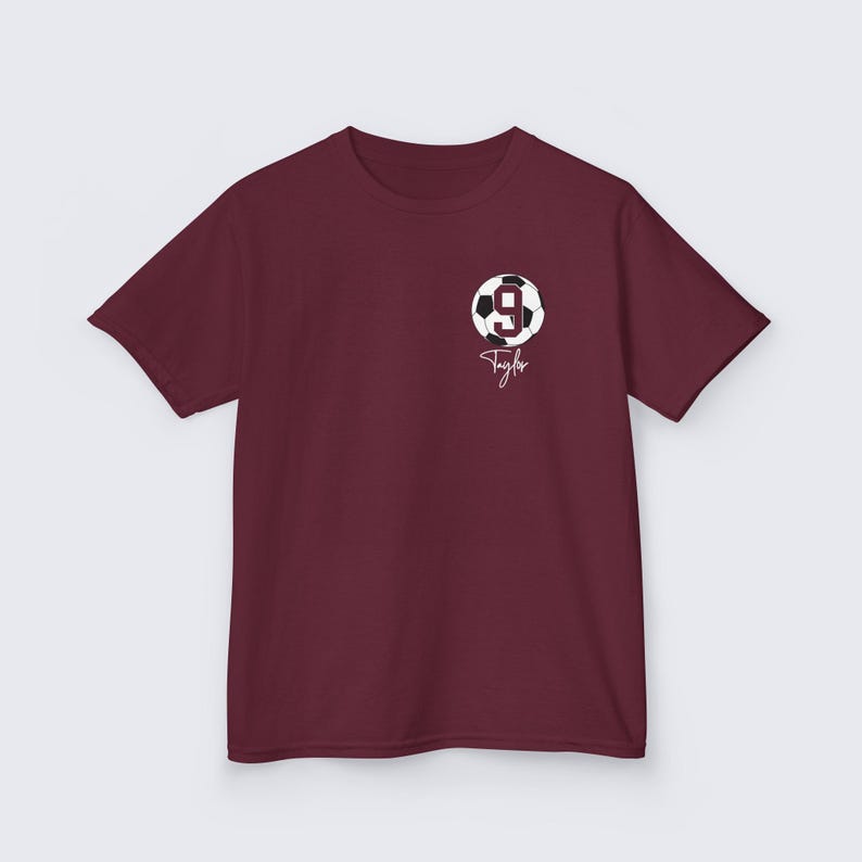 May include: Burgundy t-shirt with a white soccer ball graphic and the number 9. The name Taylor is written in white cursive below the ball.