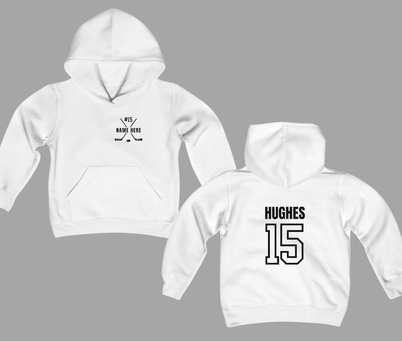 May include: White hoodie with a front pocket and hood. The front features a hockey stick graphic with the text "#15 NAME HERE". The back displays the name "HUGHES" and the number "15" in black block letters. A casual sports-themed apparel item.