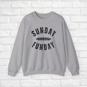 Op de afbeelding: Een grijs sweatshirt met een zwarte grafische afbeelding waarop "SUNDAY FUNDAY" staat met een voetbalnaadontwerp.