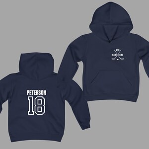 May include: Navy blue hoodie with white text and graphics. The front features a hockey stick and puck design with the text "#18 NAME HERE". The back displays the name "Peterson" above the number "18".