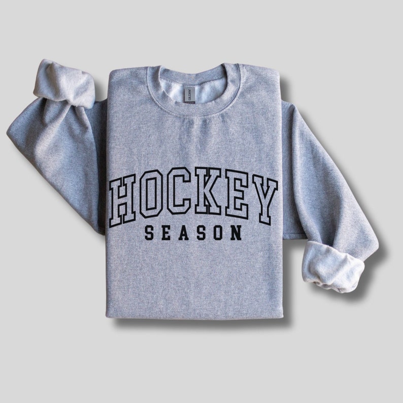Pu&ograve; includere: Una felpa grigia con il testo "HOCKEY SEASON" in lettere nere con contorno.