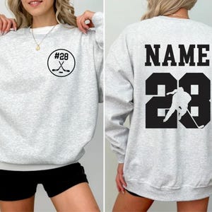 Custom hockey sweatshirt featuring a personalized hockey player name and number design on the back as well as jersey number on the front design.  Also, choose from a variety of hockey player silhouettes to further customize this hockey sweater