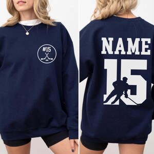 Custom hockey sweatshirt featuring a personalized hockey player name and number design on the back as well as jersey number on the front design.  Also, choose from a variety of hockey player silhouettes to further customize this hockey sweater