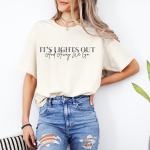 Puede incluir: Una camiseta blanca con el texto "IT'S LIGHTS OUT And Away We Go" impreso en negro.