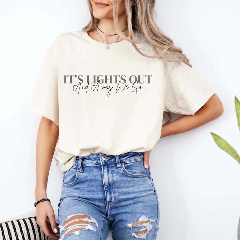 Puede incluir: Una camiseta blanca con el texto "IT'S LIGHTS OUT And Away We Go" impreso en negro.