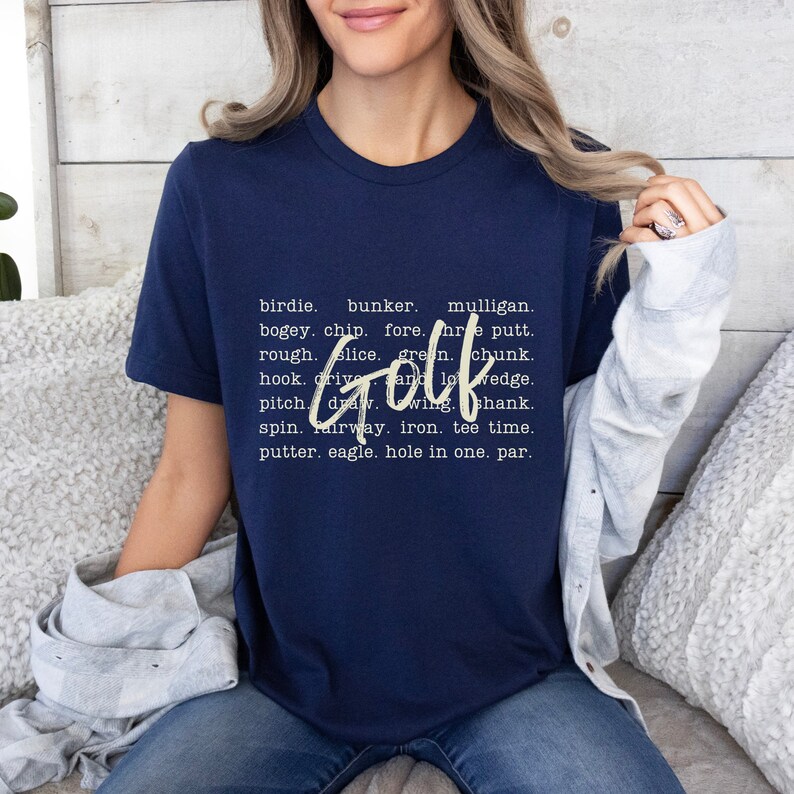 K&ouml;nnte beinhalten: Marineblaues T-Shirt mit wei&szlig;em Text, der lautet "birdie. bunker. mulligan. bogey. chip. fore. hole putt. rough. slice. green. chunk. Golf hook. drive. and lowedge. pitch. draw. wing. shank. spin. fairway. iron. tee time. putter. eagle. hole in one. par."