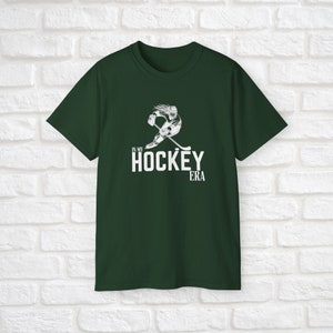 Puede incluir: Una camiseta verde oscuro con un gr&aacute;fico blanco de un jugador de hockey patinando y un texto blanco que dice "In My Hockey Era".