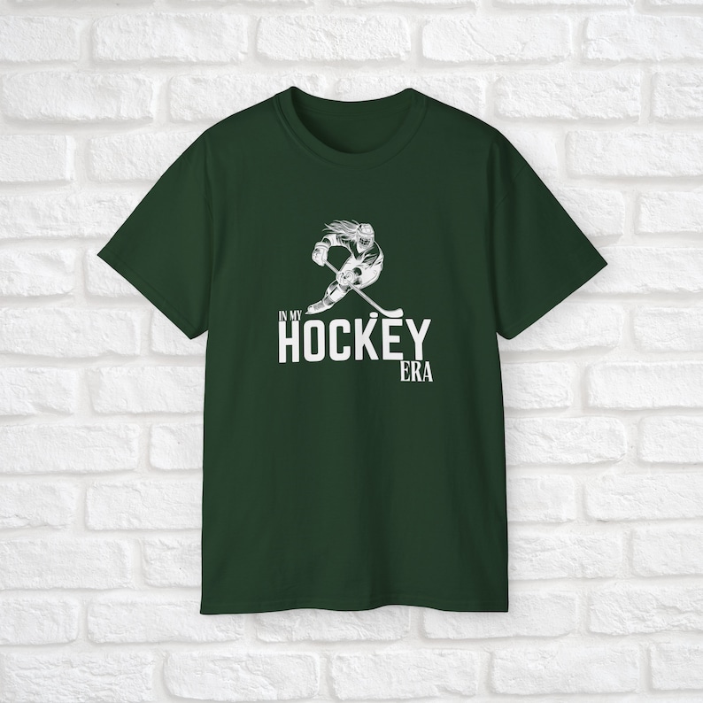 Puede incluir: Una camiseta verde oscuro con un gr&aacute;fico blanco de un jugador de hockey patinando y un texto blanco que dice "In My Hockey Era".