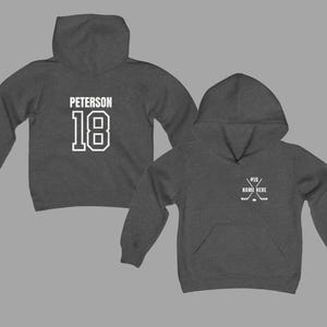 May include: Two charcoal gray hoodies. One displays "PETERSON" and the number "18" in white block letters. The other hoodie has a hockey stick graphic and the text "#18 NAME HERE" in white. Both hoodies have a front pocket and a hood.