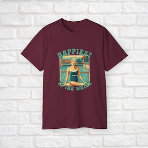 May include: A maroon t-shirt with a retro-style graphic of a woman in a swimsuit sitting by a pool. The graphic says "Happiest in the water".