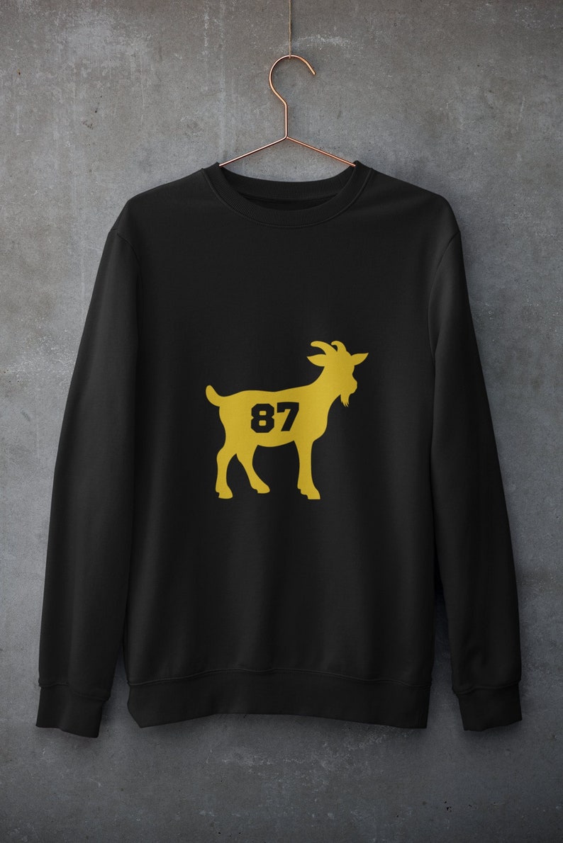 K&ouml;nnte beinhalten: Schwarzer Pullover mit einer goldenen Ziegen-Silhouette und der Nummer 87, die auf die Seite der Ziege gedruckt ist.