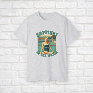 May include: A gray t-shirt with a vintage-style graphic of a woman in a swimming pool. The graphic says "Happiest in the water".