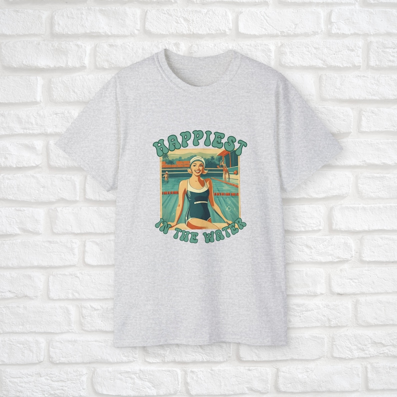 May include: A gray t-shirt with a vintage-style graphic of a woman in a swimming pool. The graphic says "Happiest in the water".