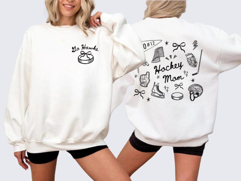 Woman wearing a crewneck sweatshirt with “Hockey Mom” doodle graphic on the back and personalized team name "Go Hawks" and player number "12" on the front; casual hockey game day outfit for moms.