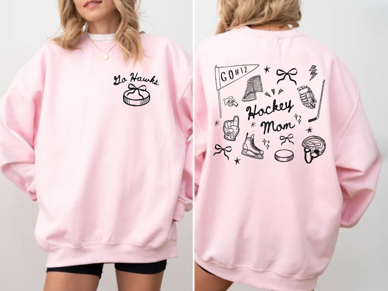 Woman wearing a crewneck sweatshirt with “Hockey Mom” doodle graphic on the back and personalized team name "Go Hawks" and player number "12" on the front; casual hockey game day outfit for moms.