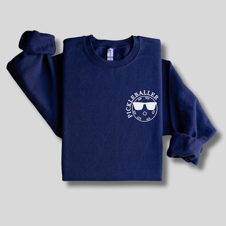 May include: A navy blue sweatshirt with a white circle graphic that says "Pickleballer" with a pickleball and sunglasses inside the circle.